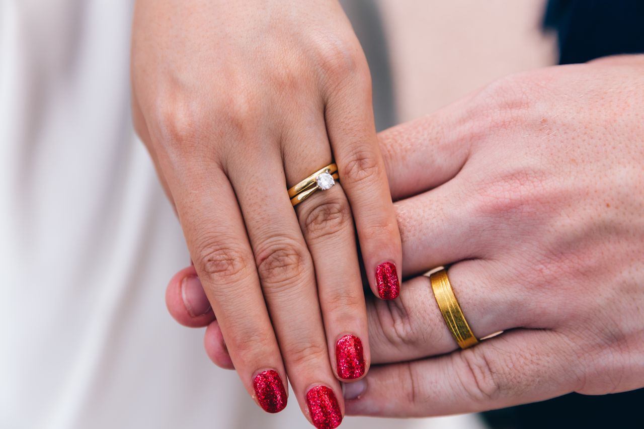 gallery-2 A close-up photo of a couple's hands showing wedding and engagement rings.