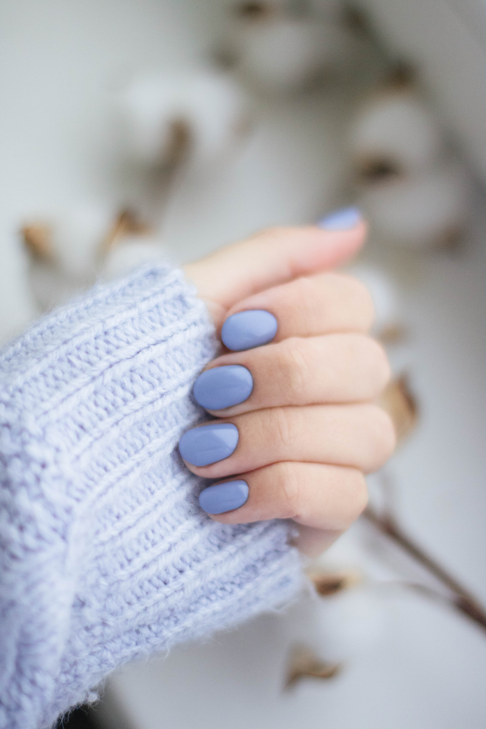 gallery-1 A close-up of a woman's hand with purple manicured nails and knitwear, showcasing trendy fashion.