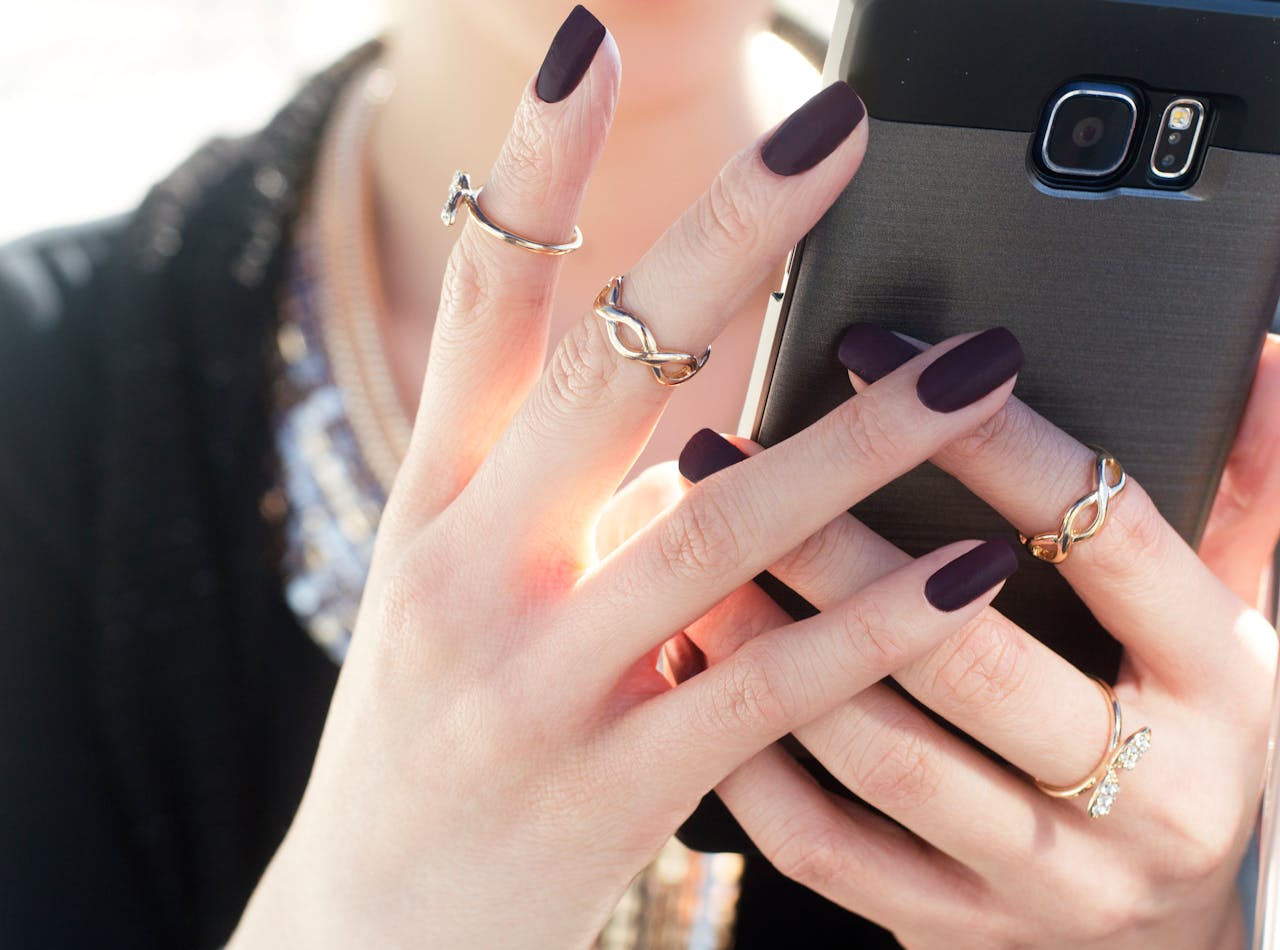 about-01 Close-up of a woman with manicured nails and rings holding a smartphone, showcasing fashion elegance.