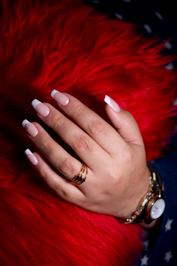 services-03 Close-up of a hand with French manicure adorned with rings and a gold watch.