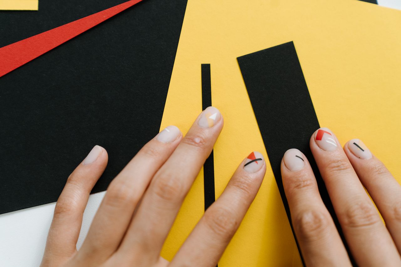 hero-img-02 Close-up of modern nail art with geometric shapes on a yellow and black paper collage.